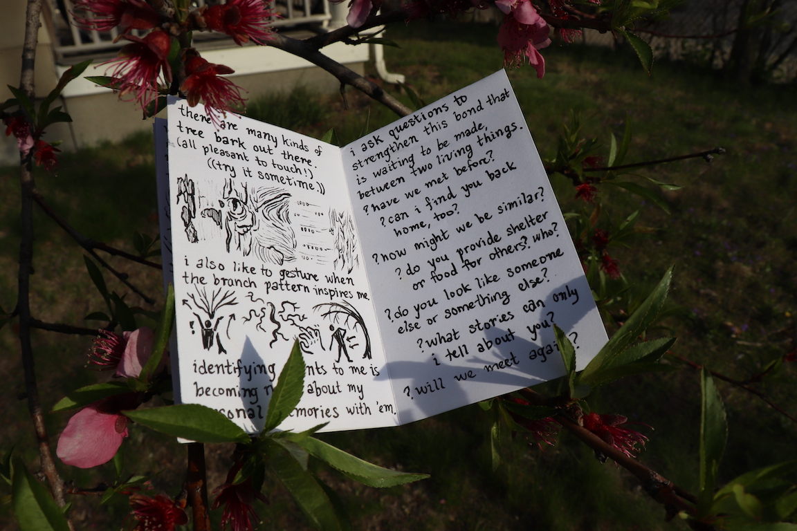 Two hands hold 'Articulations' open to a spread with a high-contrast photo, a hand-written journal entry, and an ink drawing of a leaf pile
