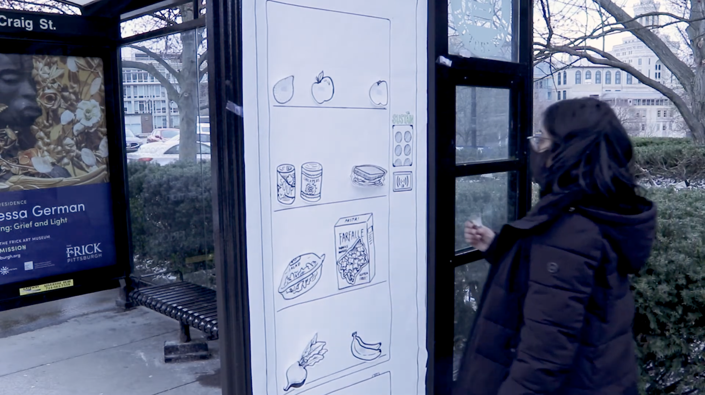 A young woman in a face mask and coat, holding a plastic card, approaches a life-size hand-drawn model of a Sustain fridge that is posted on the side of a Pittsburgh bus stop