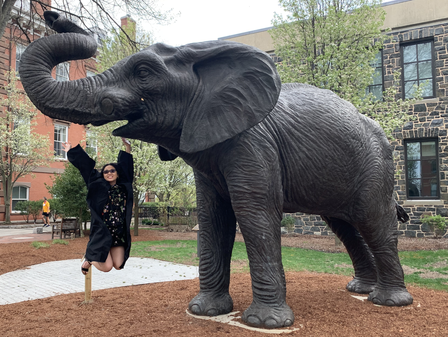 A photo of Martina wearing a black graduation cap and gown, in front of a large elephant statue (Jumbo, the Tufts mascot)